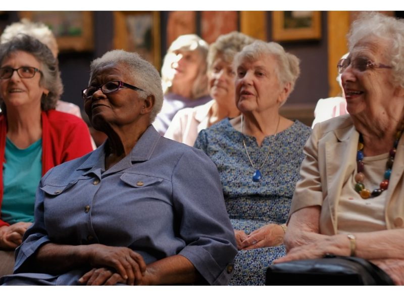 An audience of seated older people in a gallery at the Fitzwilliam Museum. Some are smiling