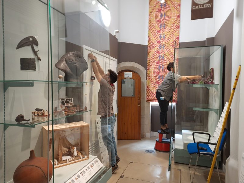 2 people standing and placing objects on to shelves in glass cabinets