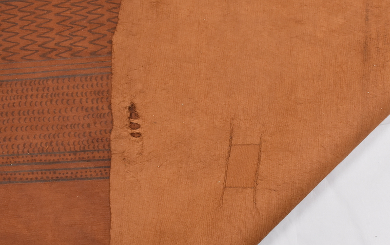 A close-up of a folded piece of barkcloth showing stitched repairs on the reverse side