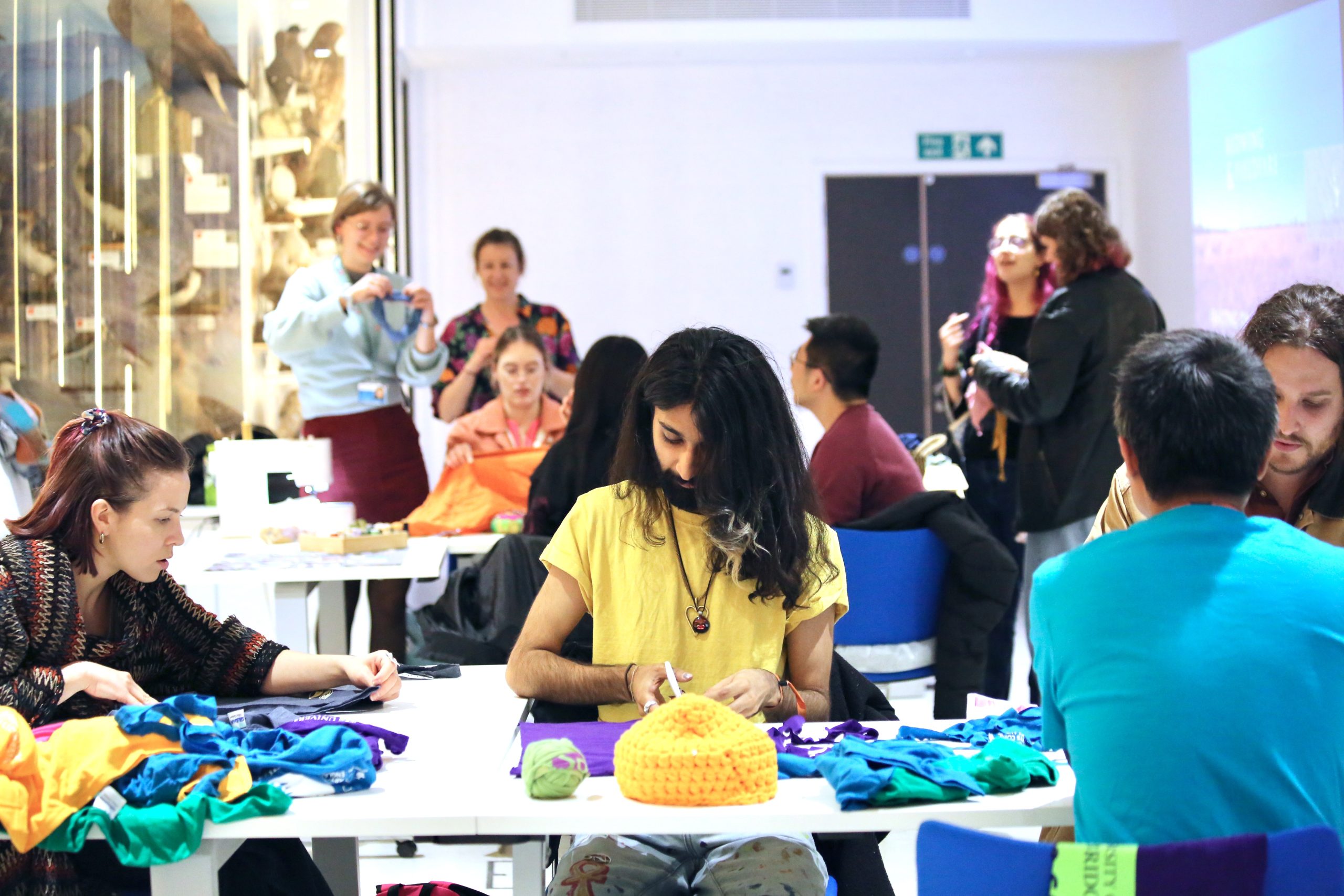 Groups of people sitting at tables using assorted fabric and wool to make clothing items