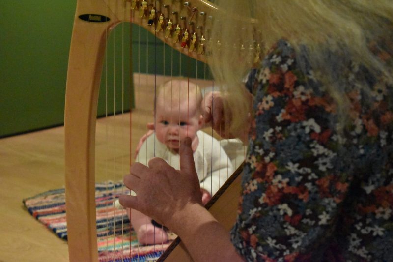 Image of a seated baby as seen through the strings of a harp