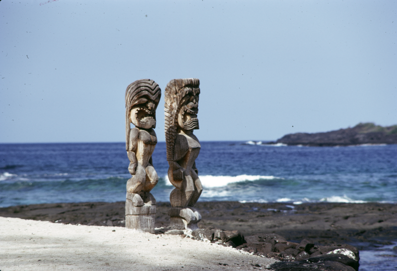 2 ornate wooden carvings on rocky outcrop facing sea