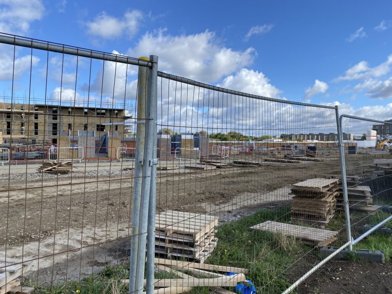 Fenced off building site with houses in the background