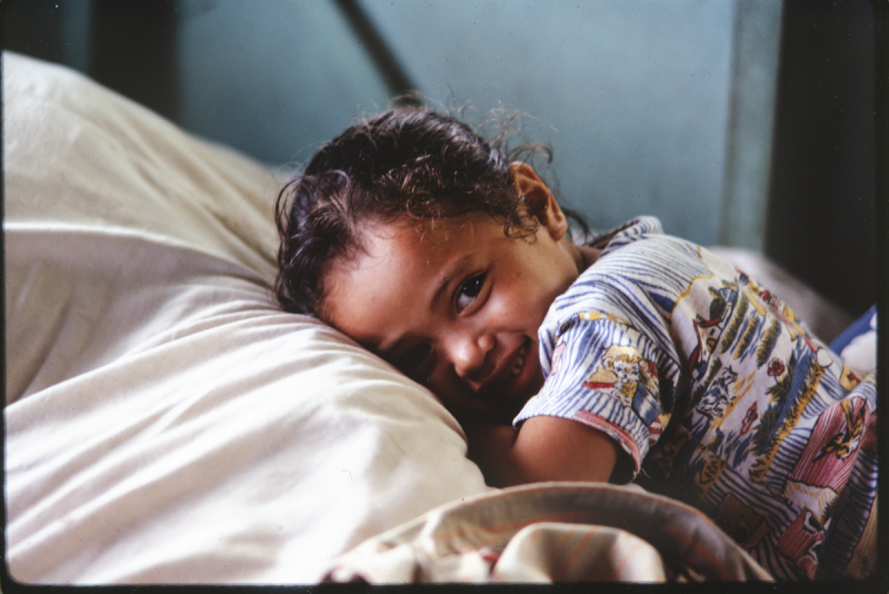 Young child wearing colourful printed dress lying on stomach and smiling at camera