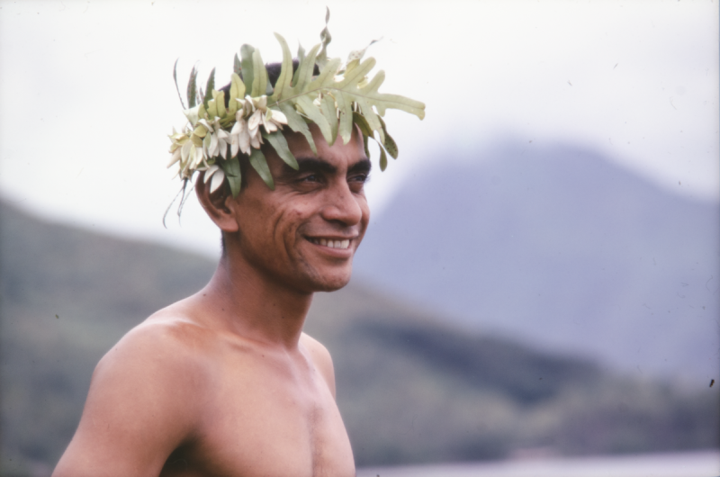 photograph of man wearing head garland standing side on to camera and smiling