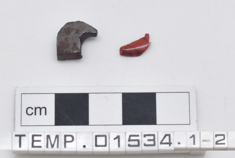 Two fragments, one of metal and one of red glass. 