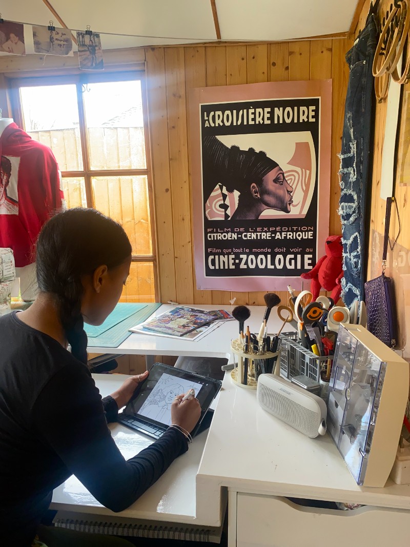 Woman sits with back to camera in an art studio. She is using an ipad to draw images