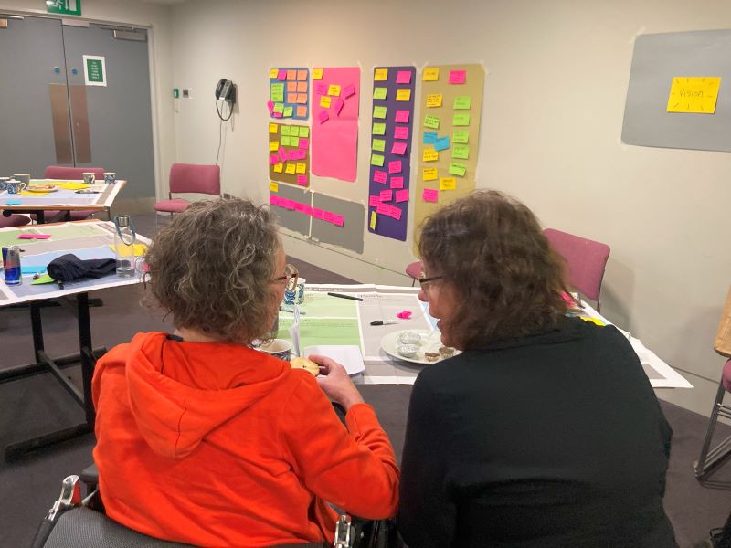 2 woman sit with back to camera at a table with pens and post-it notes