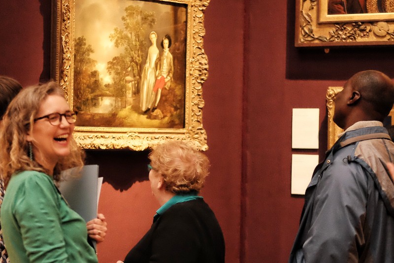 3 people in gallery looking at 18th century painting in a gold frame.