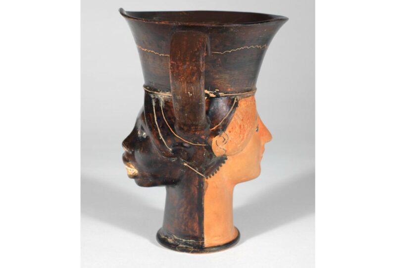 Side-on view of Greek vase showing two faces: one Black and one white