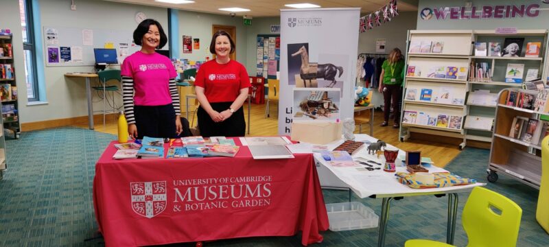 2 women stand in front of a table displaying objects from a museum handling box