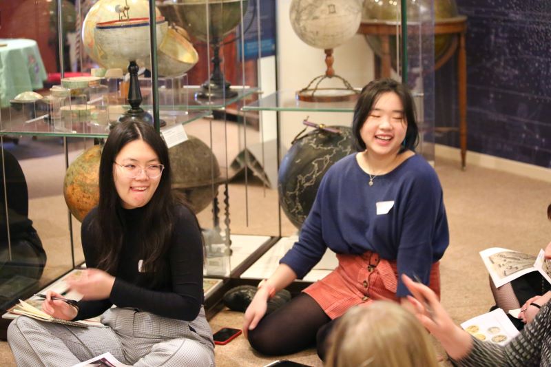 2 woman sitting on floor in front of glass display cabinets featuring model globes