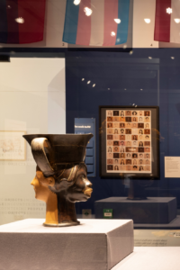 Side-on view of Greek vase showing two faces: one Black and one white, in front of another artwork.