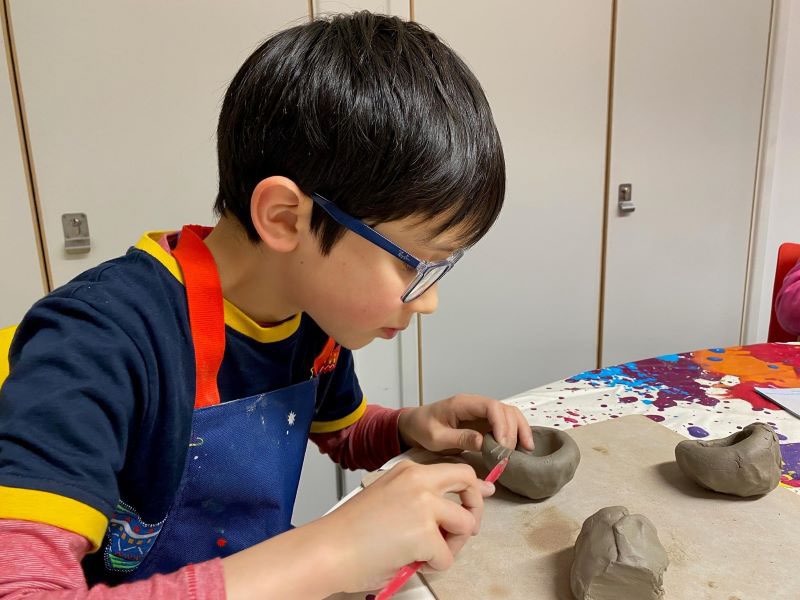 Young boy with glasses sitting making a clay pot
