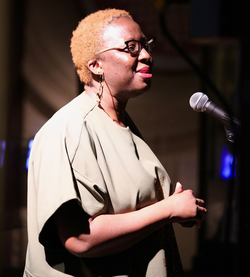 A black woman stands in front of a microphone