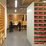 Inside the Cambridge University Herbarium - a room filled with shelves and collections storage. Two people can be seen standing at the bottom of the room.