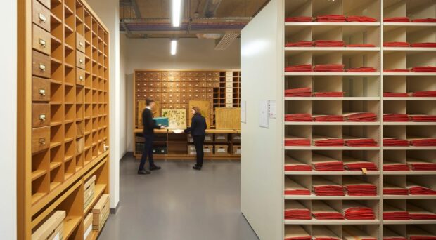 Inside the Cambridge University Herbarium - a room filled with shelves and collections storage. Two people can be seen standing at the bottom of the room.