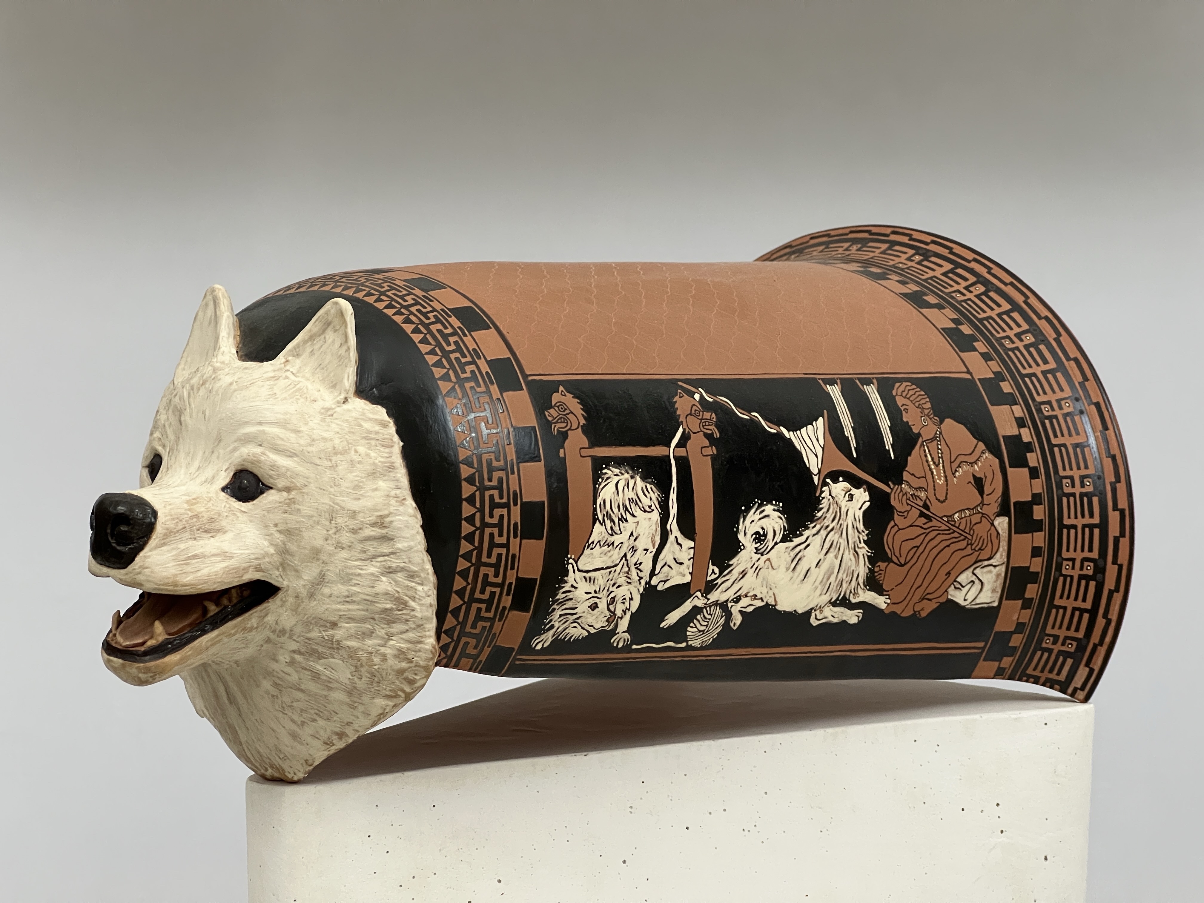 A ceramic pot originally used for carding wool, decorated with a dog's head and images of dogs with a woman working wool.