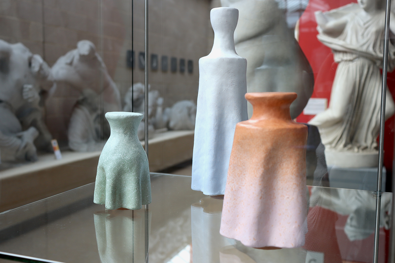 Three pink, green and orange ceramic pots, with white classical statues in the background