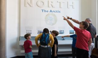 Three visitors crouched over looking at a display whilst two other visitors point of into the distance 