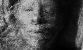 Black and white image of a woman's face beneath a linen cloth. Her eyes are closed.