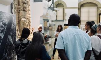 A group of people gathered around a museum object listening to an educator 