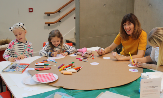 Two children and an adult at a table with a range of craft materials on a table in front of them.