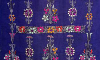 Detail of a blue dress with multi-coloured embroidery throughout. 