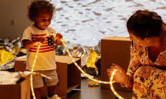 A young child holding a string of lights with an adult holding the other end.
