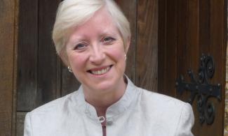 A woman with white hair and a white coat smiling into the camera