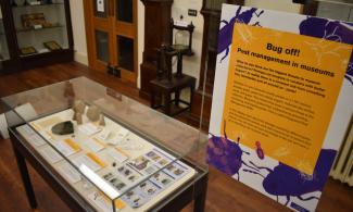 Orange and purple text panel beside a museum desk case with objects and labels.