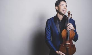 A man in a blue suit holding a violin and looking out of frame