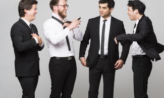 Four men in black suits standing together and laughing