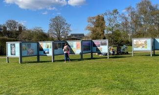 A series of display boards show photos from gardens, displayed on grass in a garden with a blue sky.