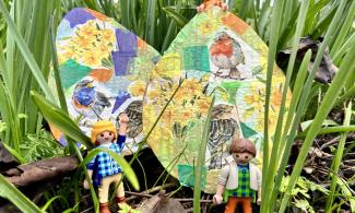 Two playmobile toy men next to collaged Easter eggs in grass.