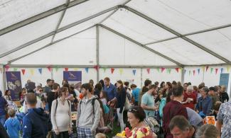A tent decked with birghtly coloured bunting and filled with people of all ages.