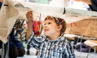 alt="a young child plays with string and cloth in the museum"