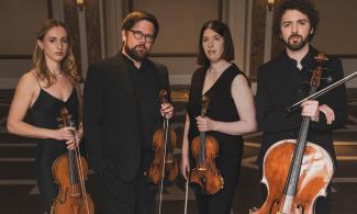 Four people, all dressed in black, staring directly at the camera, each holding a string musical instrument.