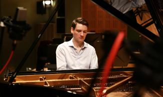 A man sits playing at an open-top piano.