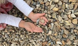 A child's hands are held above a floor of gravel, holding a few pieces of gravel.