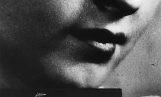 A black and white photograph of a woman's face, with a book in front of it.