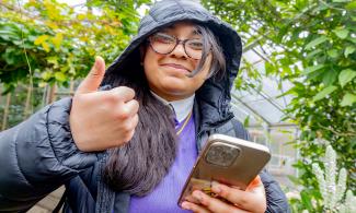 Girl wearing hood holding phone and giving thumbs up sign