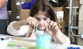 A girl making a glass lantern adding tissue paper to a jar.