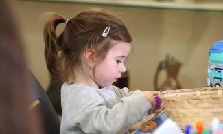 alt= "a young girl with long brown hair tied in a ponytail plays with arts and crafts supplies"