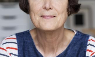 Cornelia Parker, a woman with short brown hair, wearing a navy pinafore, smiling at the camera.