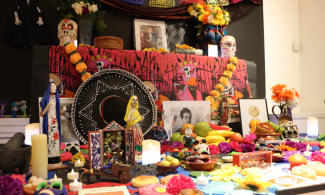 The first and second levels of a three tier altar decorated with food, flowers, skeletons, and photographs.