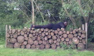 Harold Offeh lying on his front of a pile of logs.