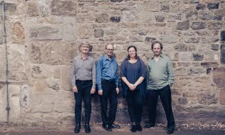Four people stood in front of an old stone building, smiling at the camera.