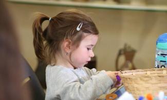 alt= "a young girl with long brown hair tied in a ponytail plays with arts and crafts supplies"