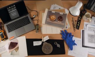 A curator’s desk featuring an astrolabe alongside research books, images, and supporting materials.
